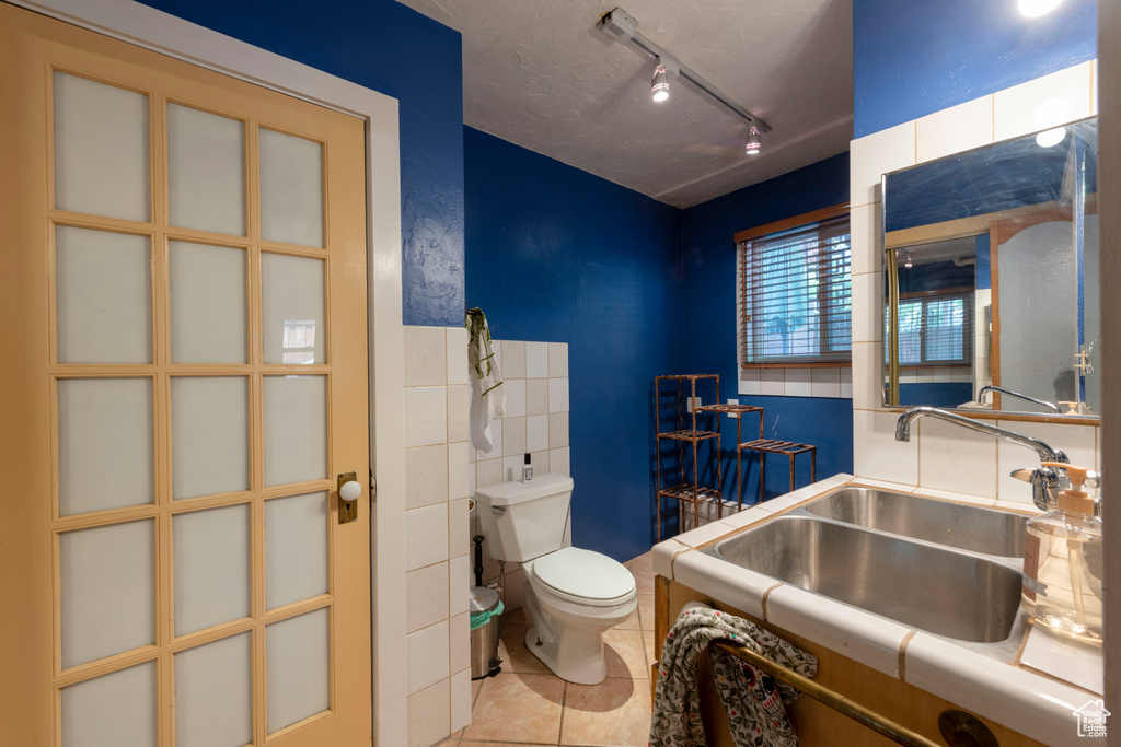 Bathroom with a sink, toilet, tile patterned flooring, track lighting, and tile walls