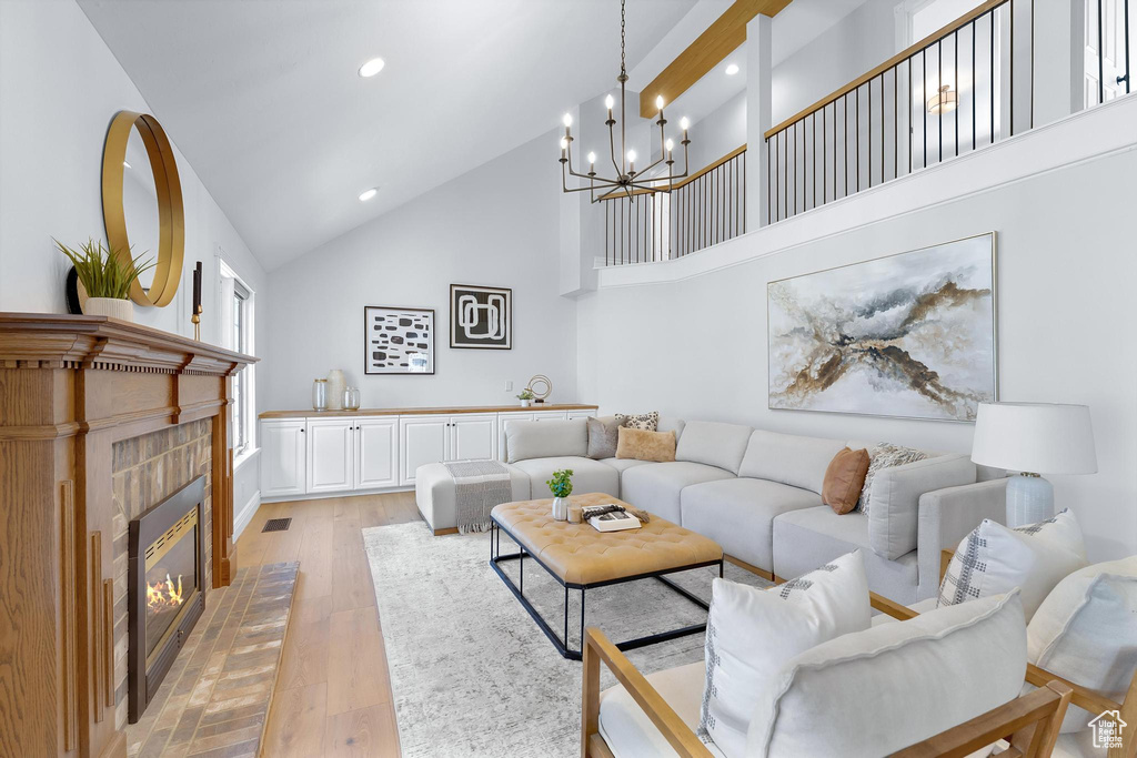 Living room featuring light wood finished floors, recessed lighting, high vaulted ceiling, a chandelier, and a tiled fireplace