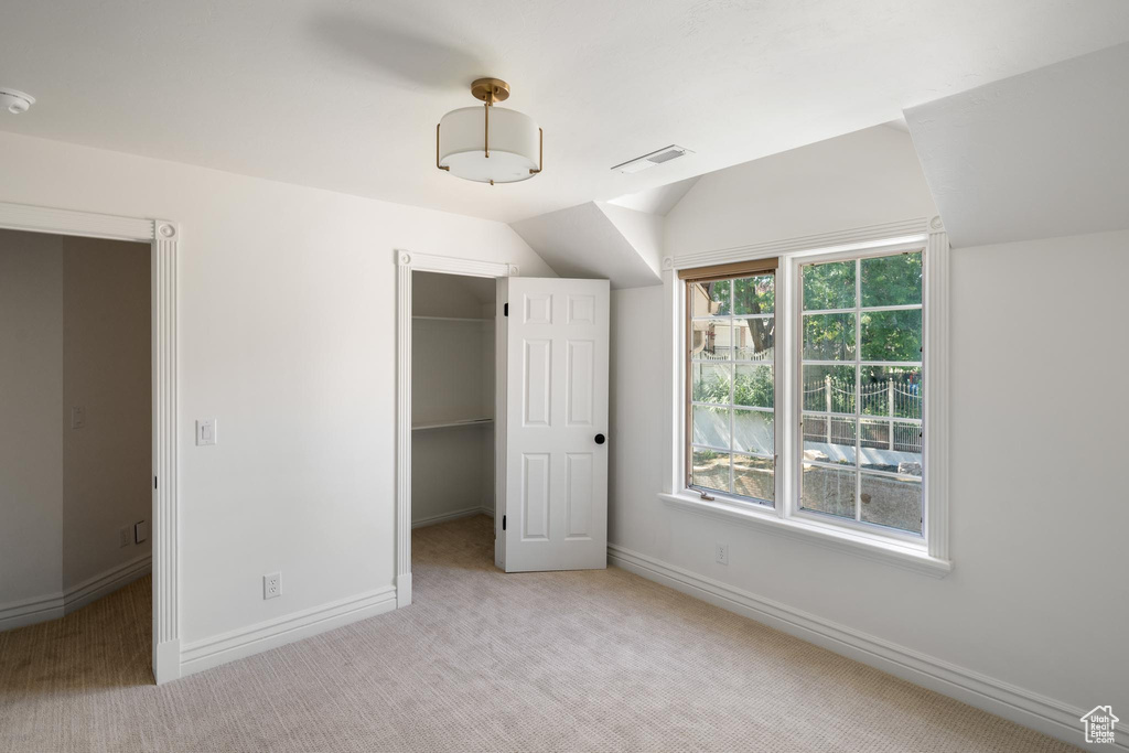 Unfurnished bedroom with light carpet, a spacious closet, vaulted ceiling, baseboards, and a closet
