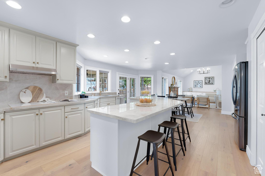 Kitchen with freestanding refrigerator, under cabinet range hood, a breakfast bar, light wood-style flooring, and recessed lighting