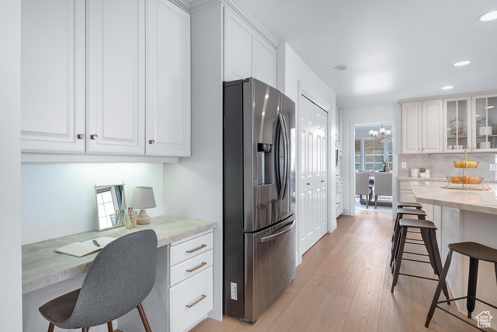 Kitchen featuring stainless steel fridge with ice dispenser, a kitchen breakfast bar, light wood-type flooring, white cabinets, and recessed lighting