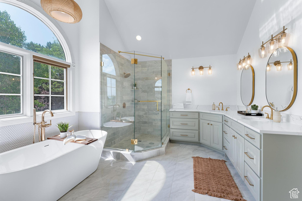 Full bathroom featuring lofted ceiling, double vanity, a stall shower, a soaking tub, and a wainscoted wall