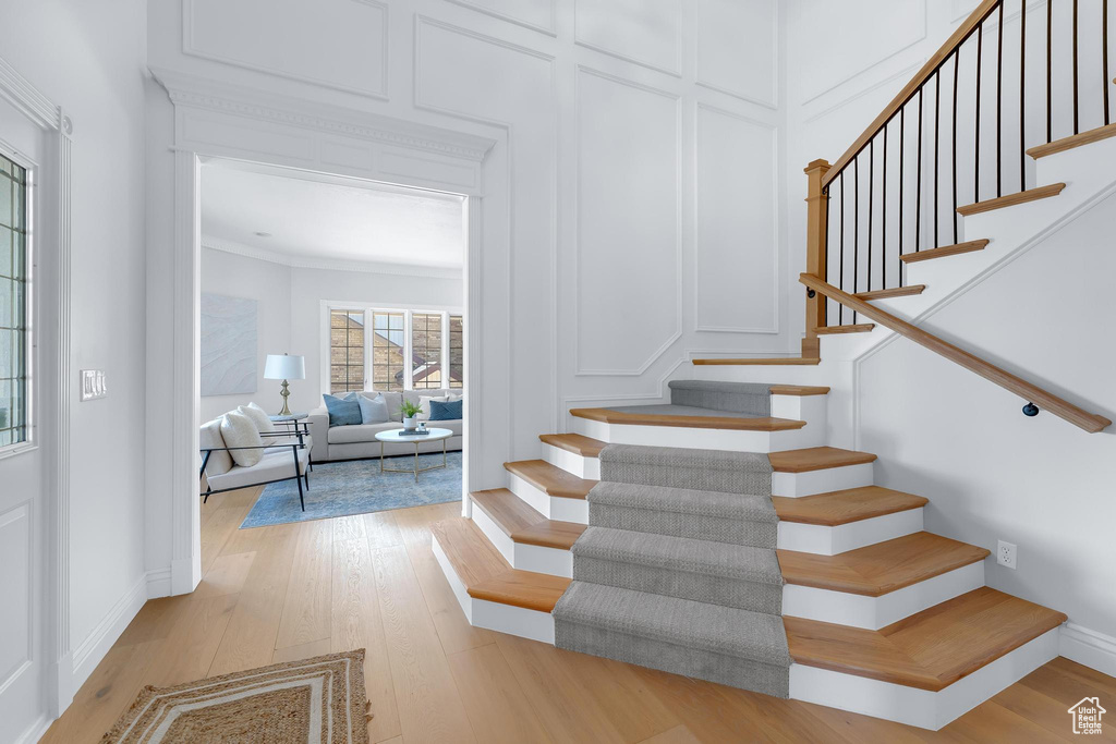 Stairs with a decorative wall, wood finished floors, and crown molding