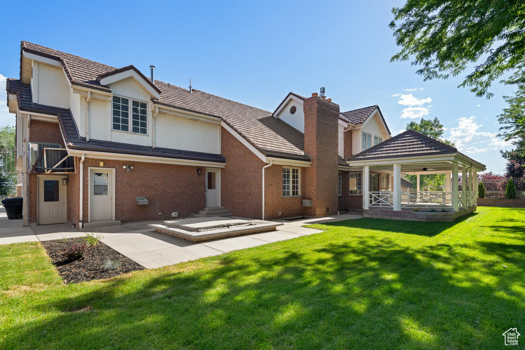 Rear view of house featuring a yard, brick siding, a chimney, stucco siding, and covered porch