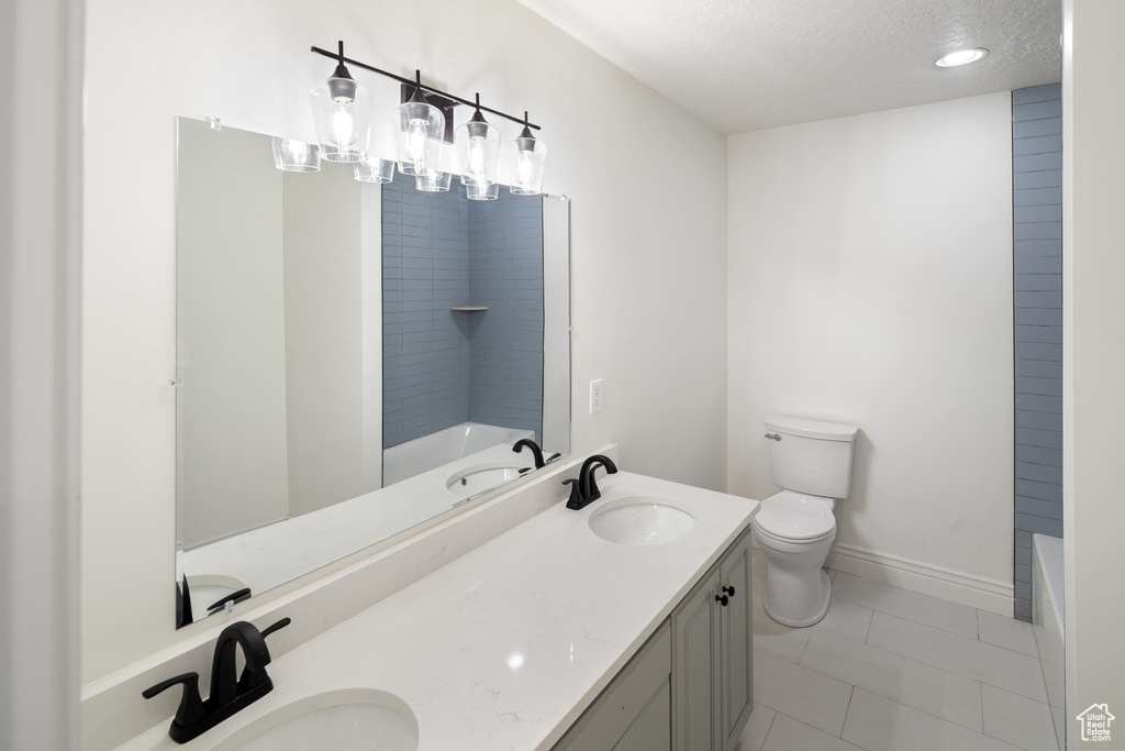 Full bathroom featuring double vanity, toilet, a textured ceiling, tile patterned flooring, and baseboards