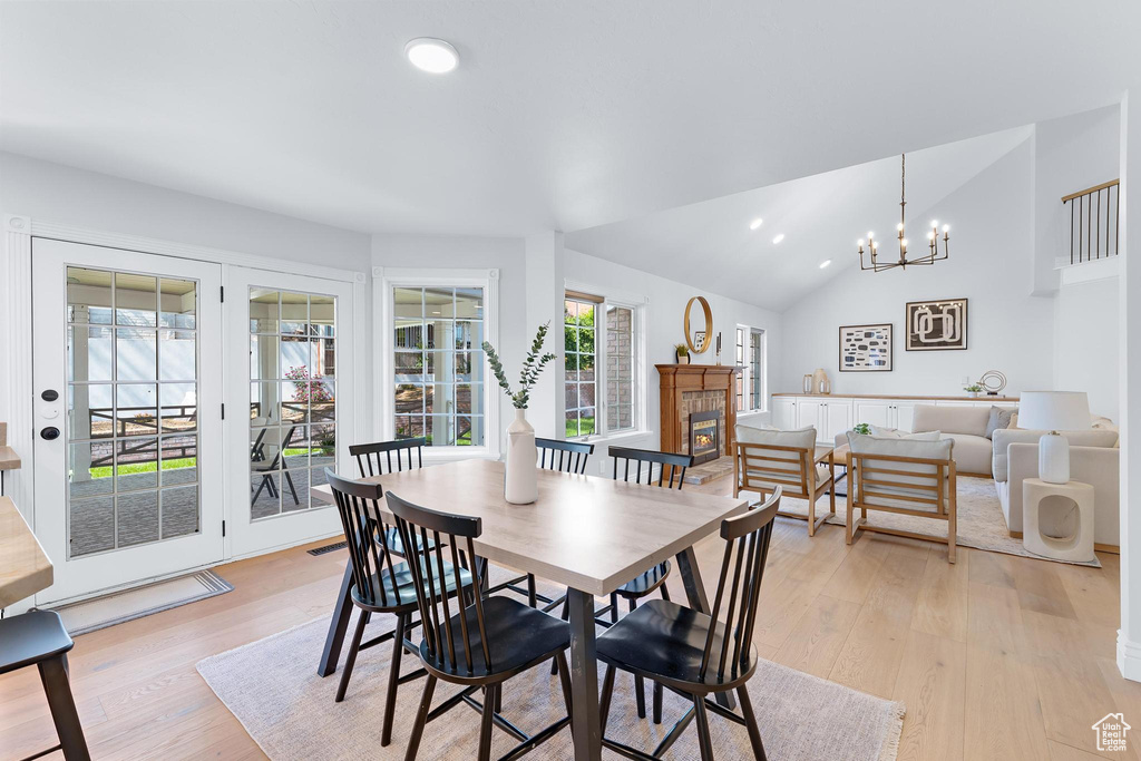 Dining area with light wood finished floors, a chandelier, a glass covered fireplace, lofted ceiling, and recessed lighting