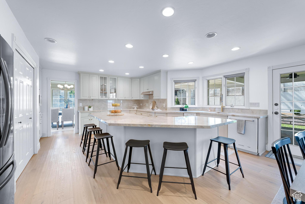 Kitchen with a kitchen island, a kitchen breakfast bar, white cabinets, backsplash, and recessed lighting