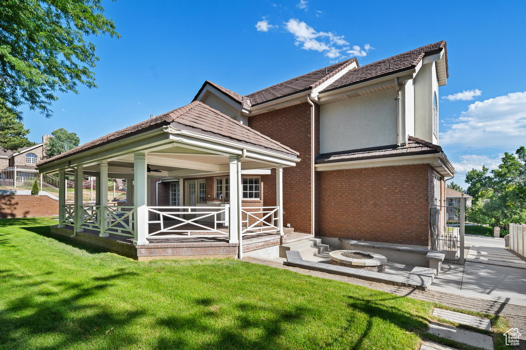Rear view of property with a yard, brick siding, an outdoor fire pit, ceiling fan, and a patio area