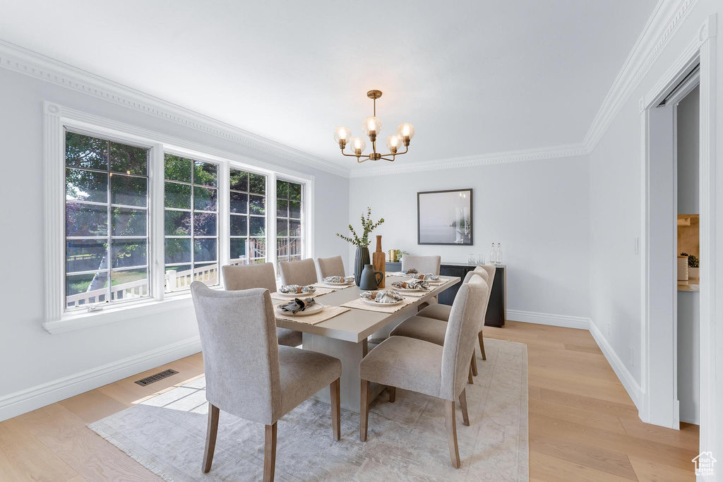 Dining area with a chandelier, ornamental molding, light wood finished floors, and baseboards