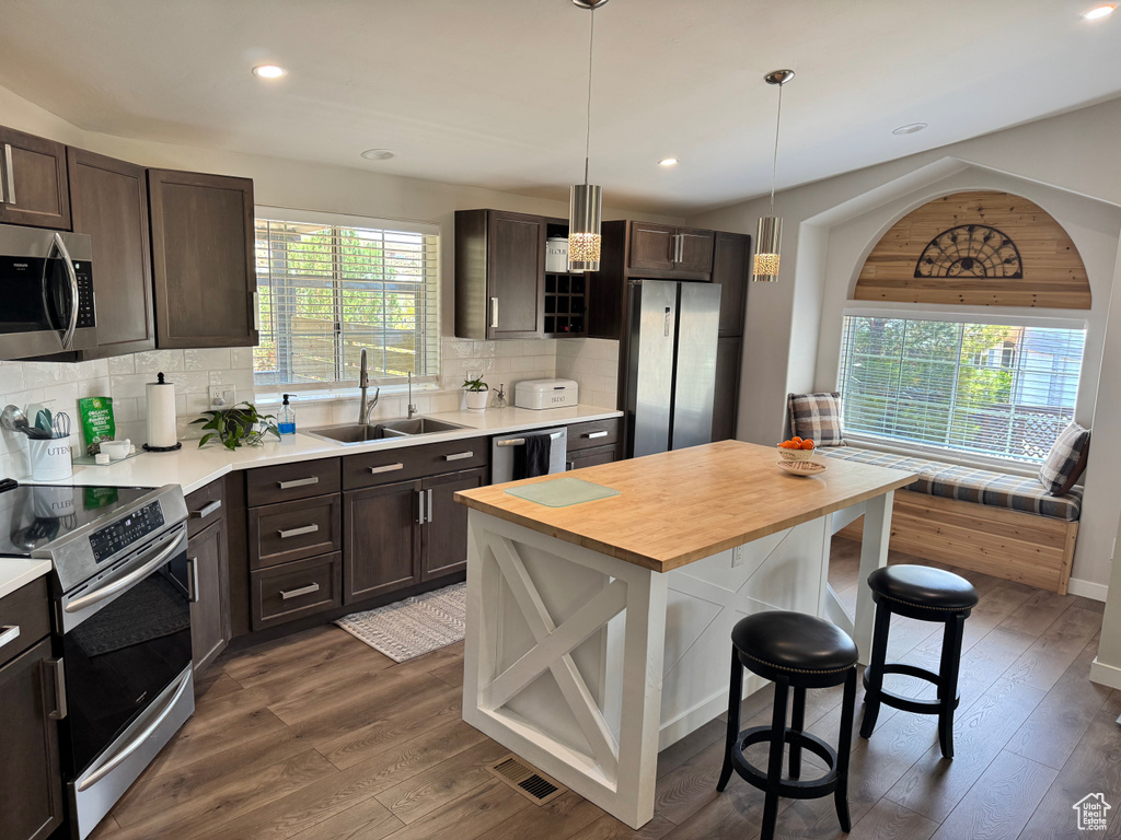 Kitchen featuring appliances with stainless steel finishes, a sink, a breakfast bar, dark brown cabinetry, and recessed lighting