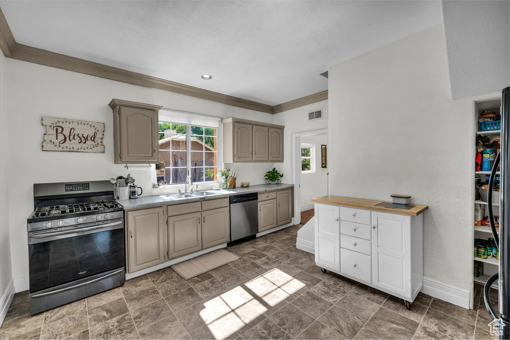 Kitchen featuring appliances with stainless steel finishes, baseboards, a sink, ornamental molding, and light countertops