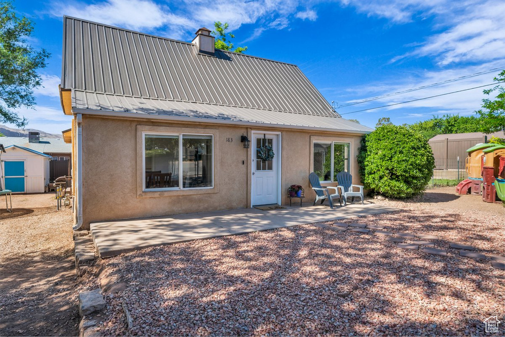Back of property featuring stucco siding, a patio area, metal roof, and a chimney