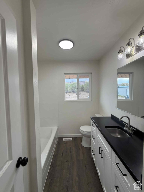 Bathroom with vanity, toilet, wood finished floors, a tub to relax in, and baseboards