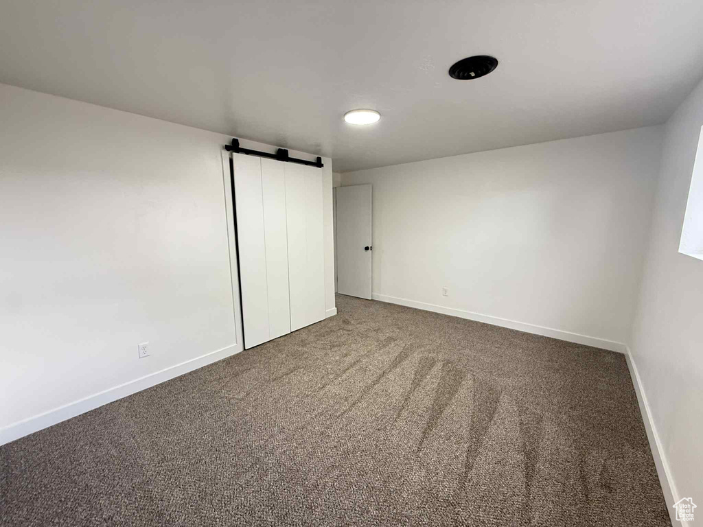 Unfurnished bedroom with a barn door, carpet, and baseboards