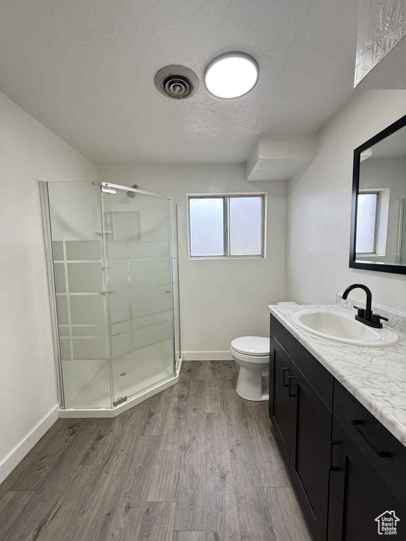 Bathroom featuring a stall shower, vanity, toilet, wood finished floors, and baseboards