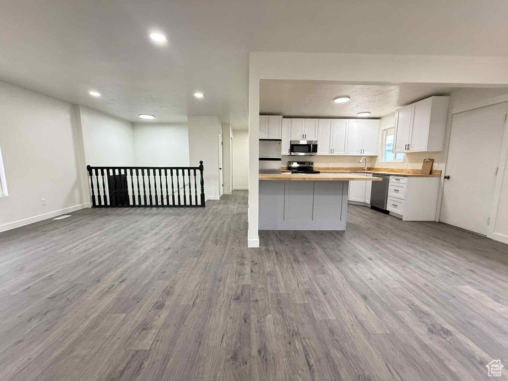 Kitchen with stainless steel appliances, open floor plan, wood finished floors, white cabinetry, and recessed lighting