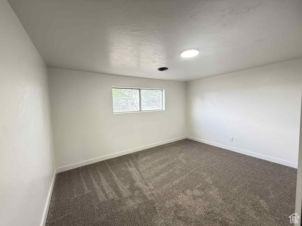 Empty room featuring baseboards and dark carpet