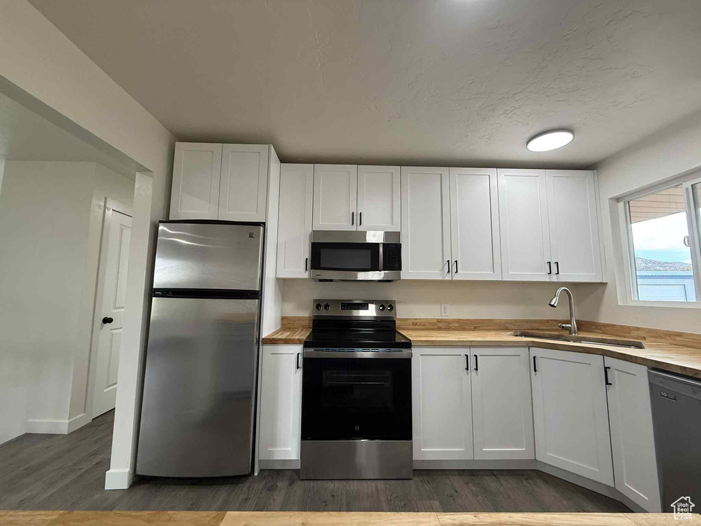 Kitchen featuring stainless steel appliances, a sink, butcher block counters, light wood-style floors, and white cabinets