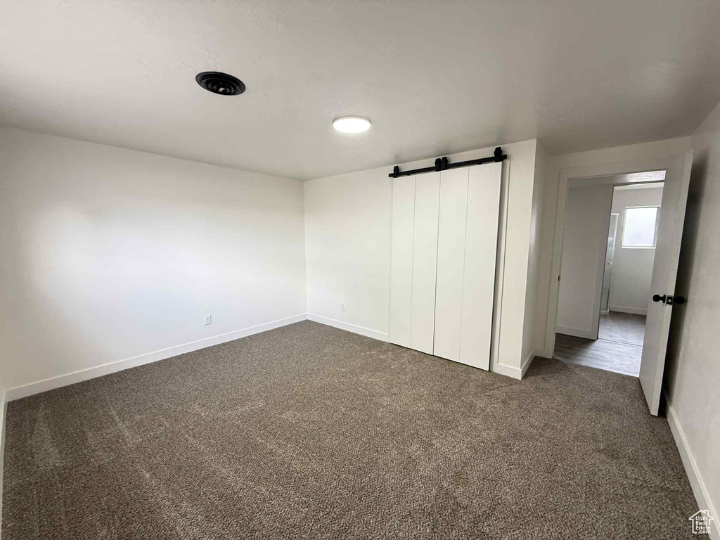 Unfurnished bedroom featuring a barn door, dark colored carpet, and baseboards