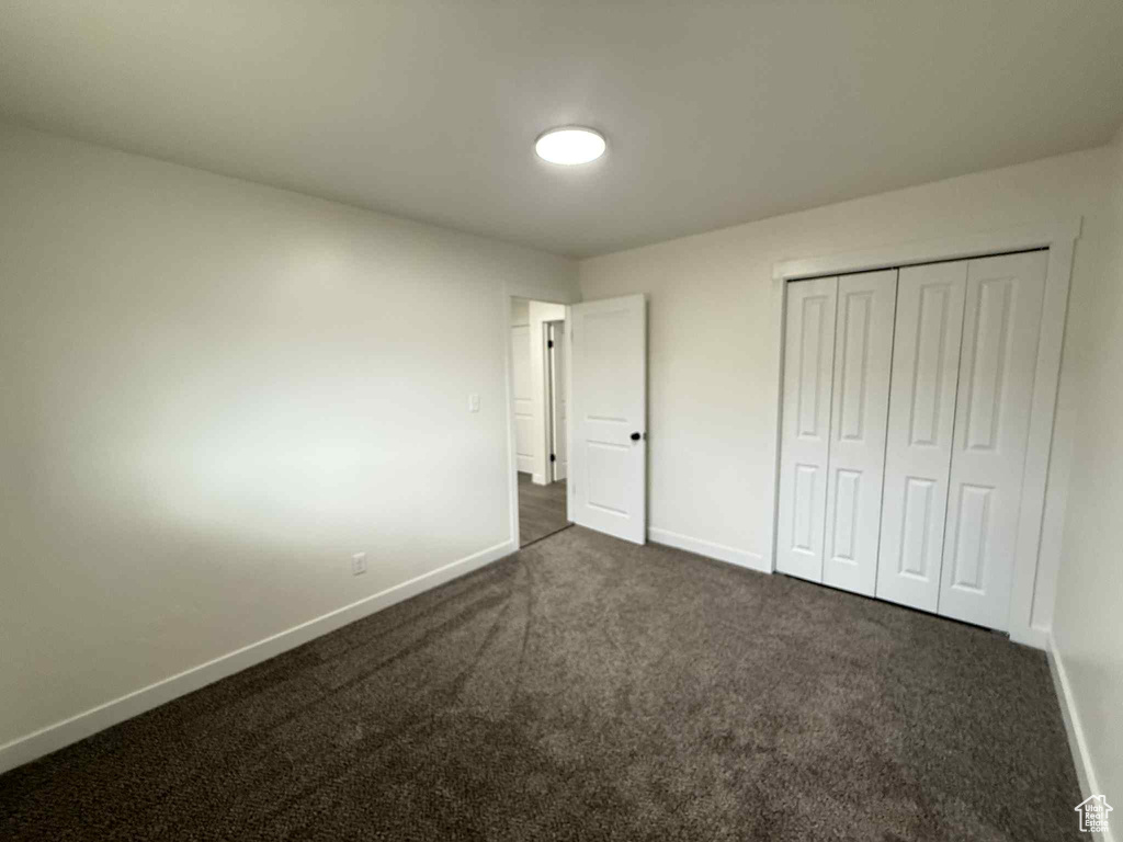Unfurnished bedroom featuring baseboards, dark carpet, and a closet