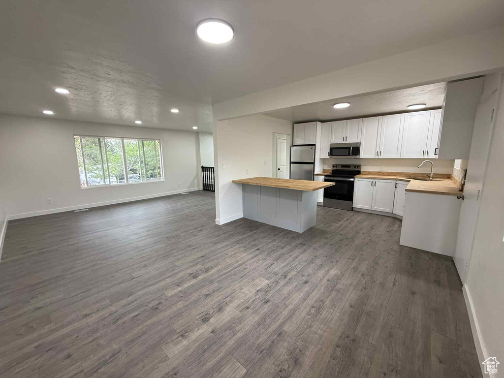 Kitchen featuring appliances with stainless steel finishes, wood counters, open floor plan, baseboards, and a peninsula