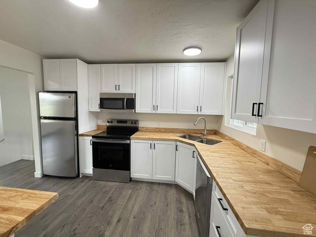 Kitchen with stainless steel appliances, a sink, dark wood-style floors, white cabinets, and wood counters