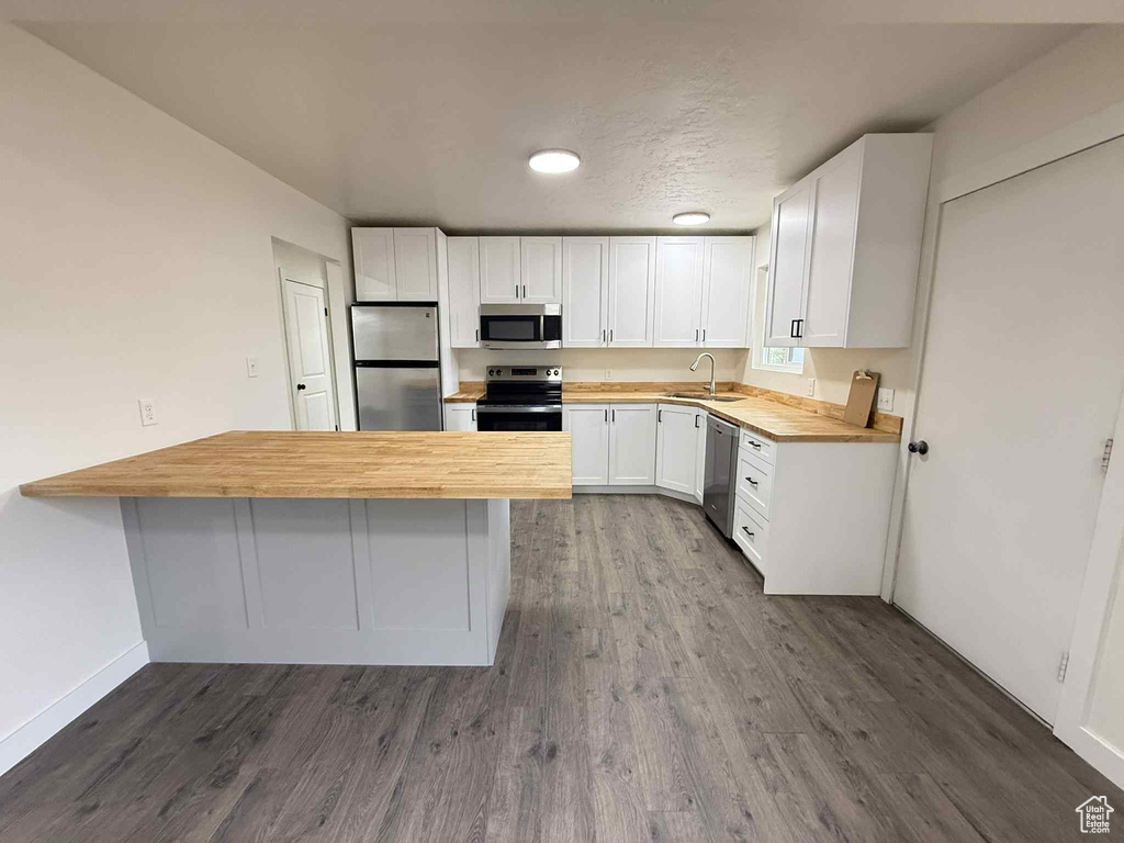 Kitchen featuring appliances with stainless steel finishes, a peninsula, wooden counters, a sink, and white cabinetry