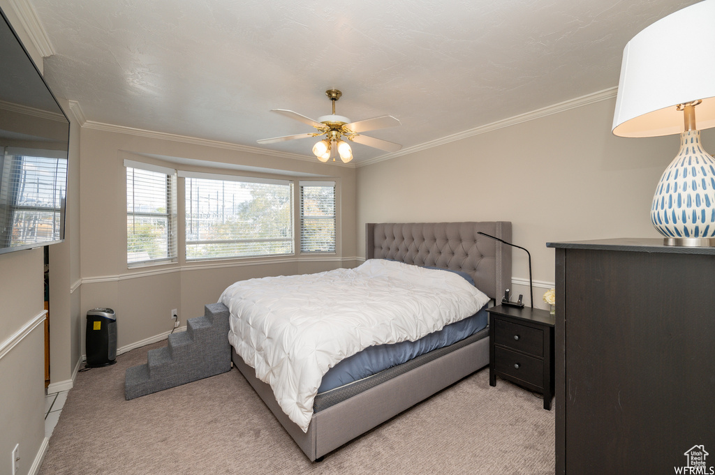 Bedroom featuring light carpet, crown molding, baseboards, and ceiling fan
