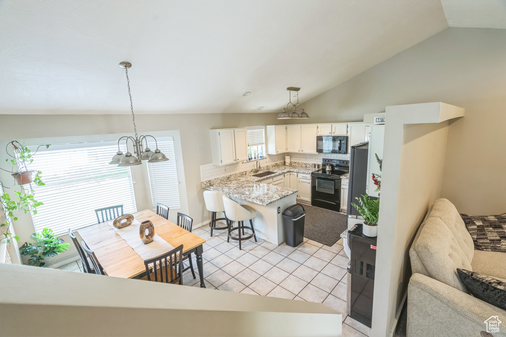 Kitchen with black appliances, a chandelier, a peninsula, vaulted ceiling, and a sink