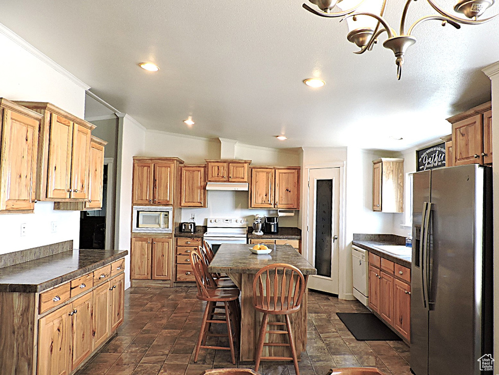 Kitchen featuring white appliances, dark countertops, under cabinet range hood, a center island, and crown molding