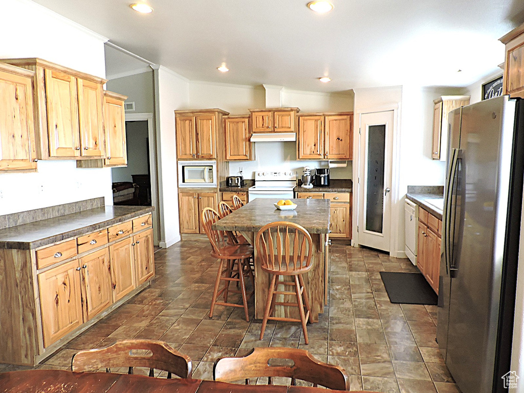 Kitchen featuring white appliances, a kitchen island, under cabinet range hood, dark countertops, and recessed lighting