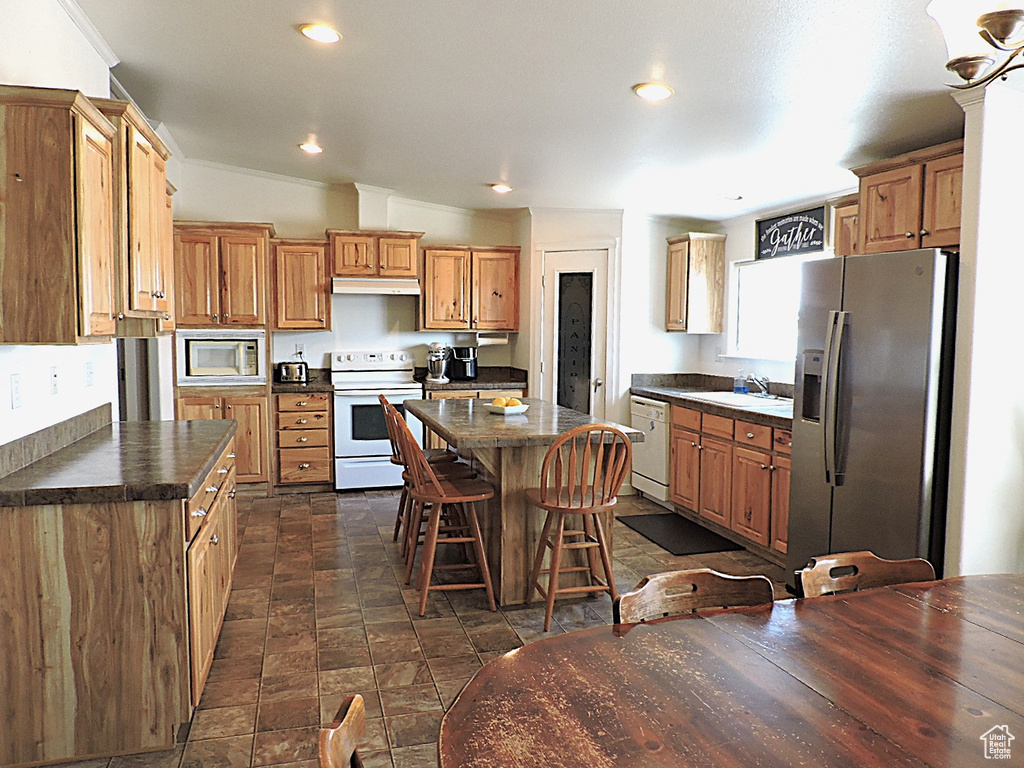 Kitchen with white appliances, dark countertops, a breakfast bar, a sink, and recessed lighting