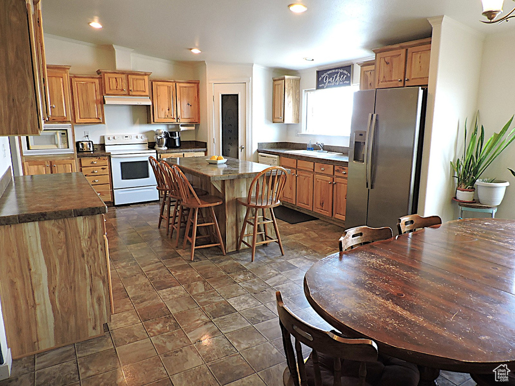 Kitchen featuring white appliances, under cabinet range hood, a sink, a kitchen island, and dark countertops