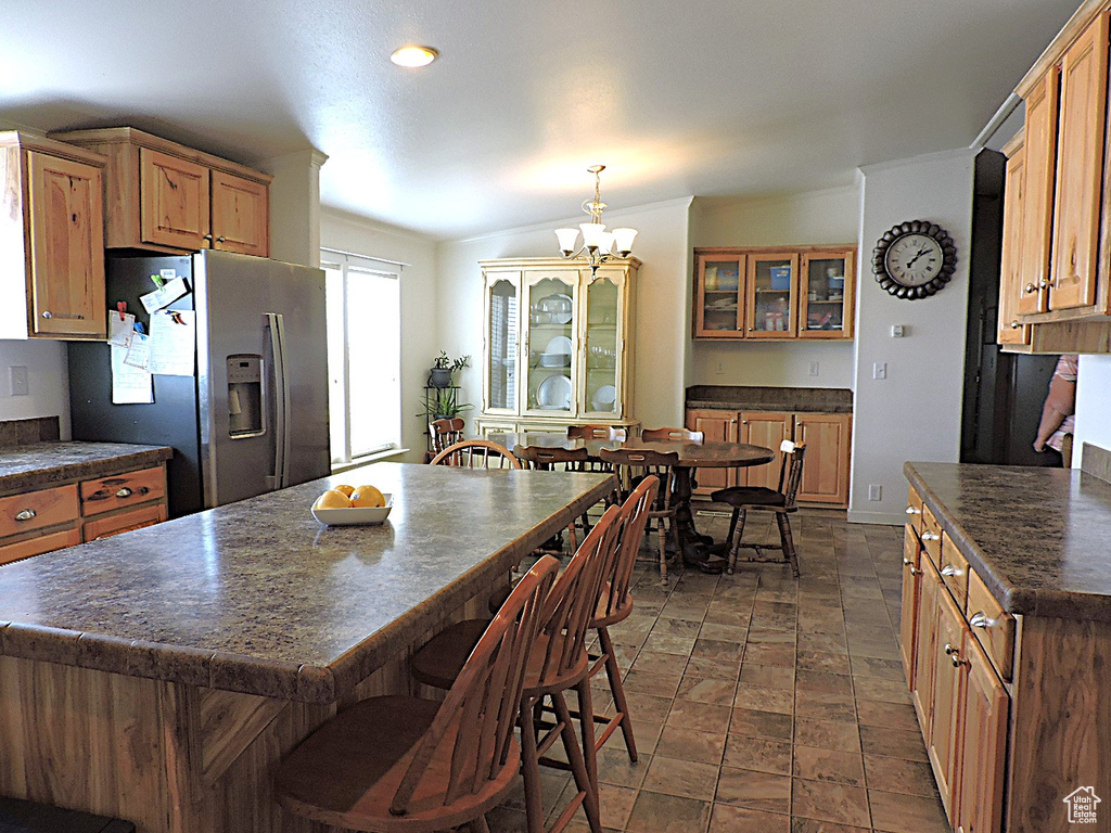 Kitchen with stainless steel refrigerator with ice dispenser, dark countertops, a chandelier, glass insert cabinets, and brown cabinets