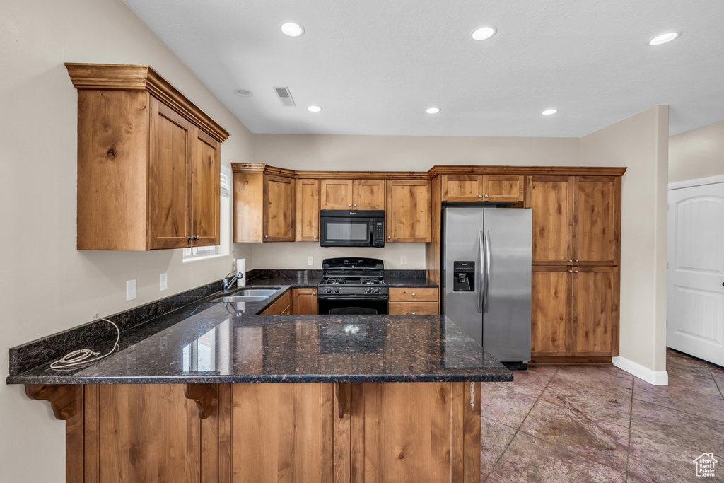 Kitchen with black appliances, a sink, a peninsula, brown cabinetry, and dark stone countertops