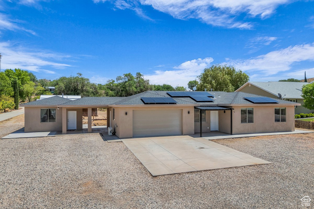 Ranch-style home featuring stucco siding, a garage, concrete driveway, solar panels, and a porch