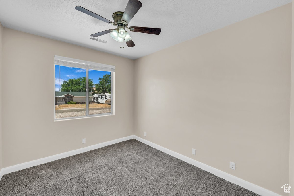 Spare room featuring baseboards, dark carpet, a ceiling fan, and a textured ceiling