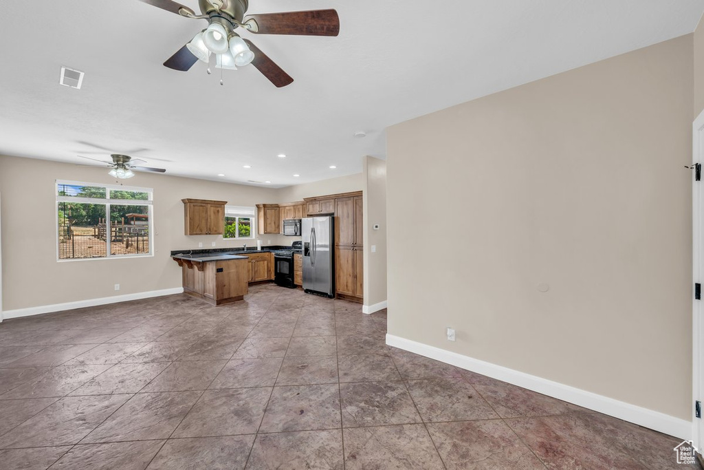 Kitchen with black appliances, open floor plan, dark countertops, a ceiling fan, and baseboards