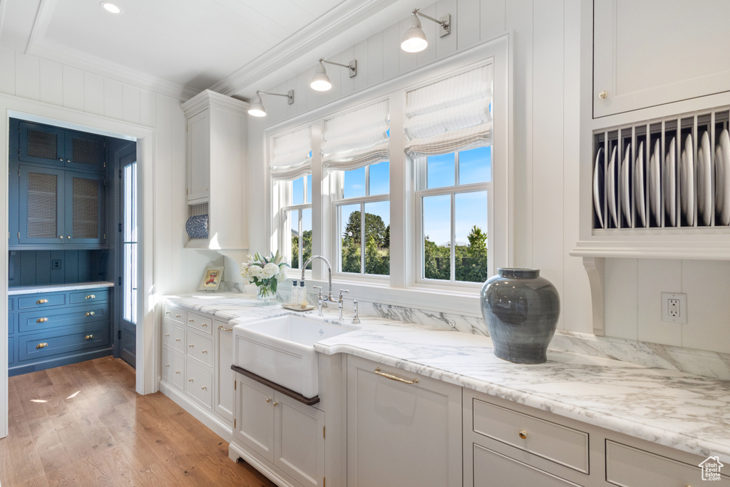 Kitchen featuring a sink, light wood finished floors, ornamental molding, white cabinetry, and light stone counters