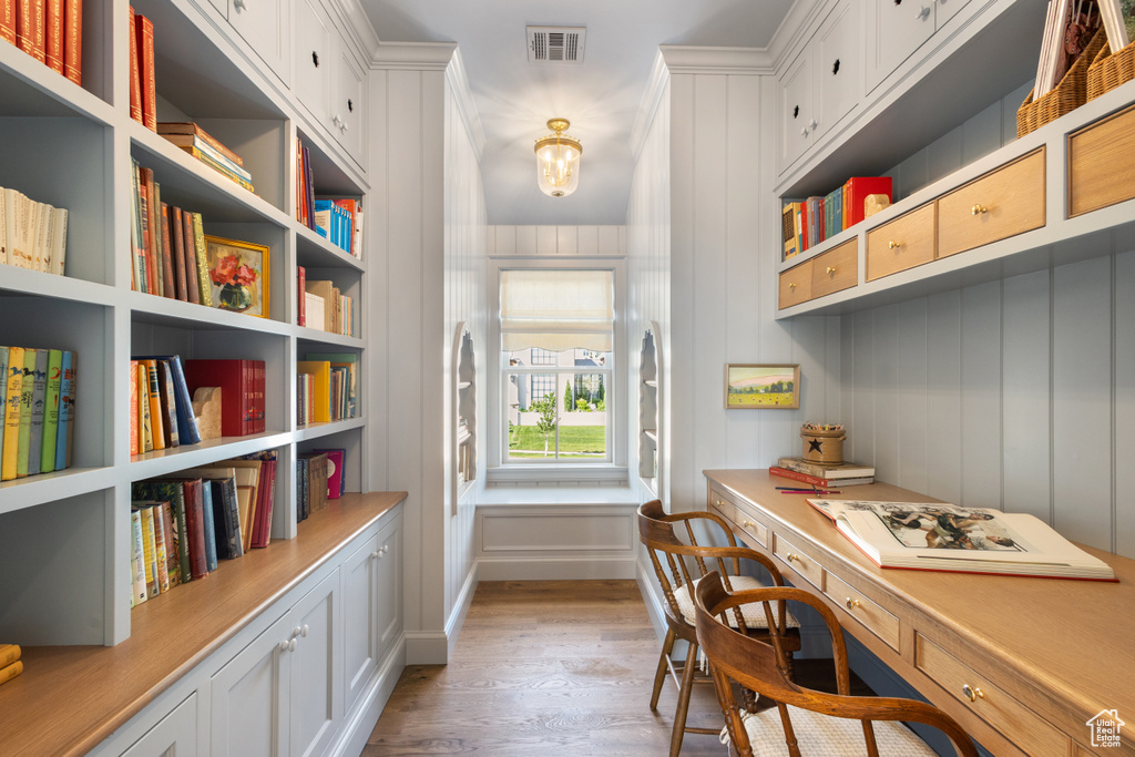 Office with light wood finished floors, built in study area, a chandelier, and a decorative wall