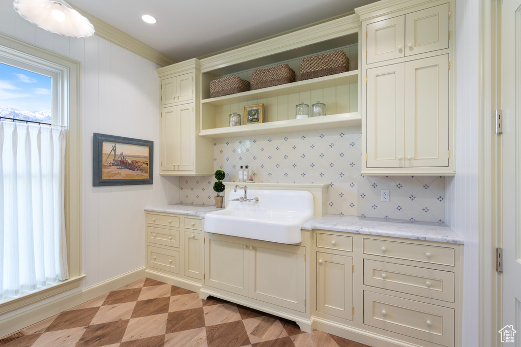 Kitchen with a sink, baseboards, open shelves, light flooring, and cream cabinetry