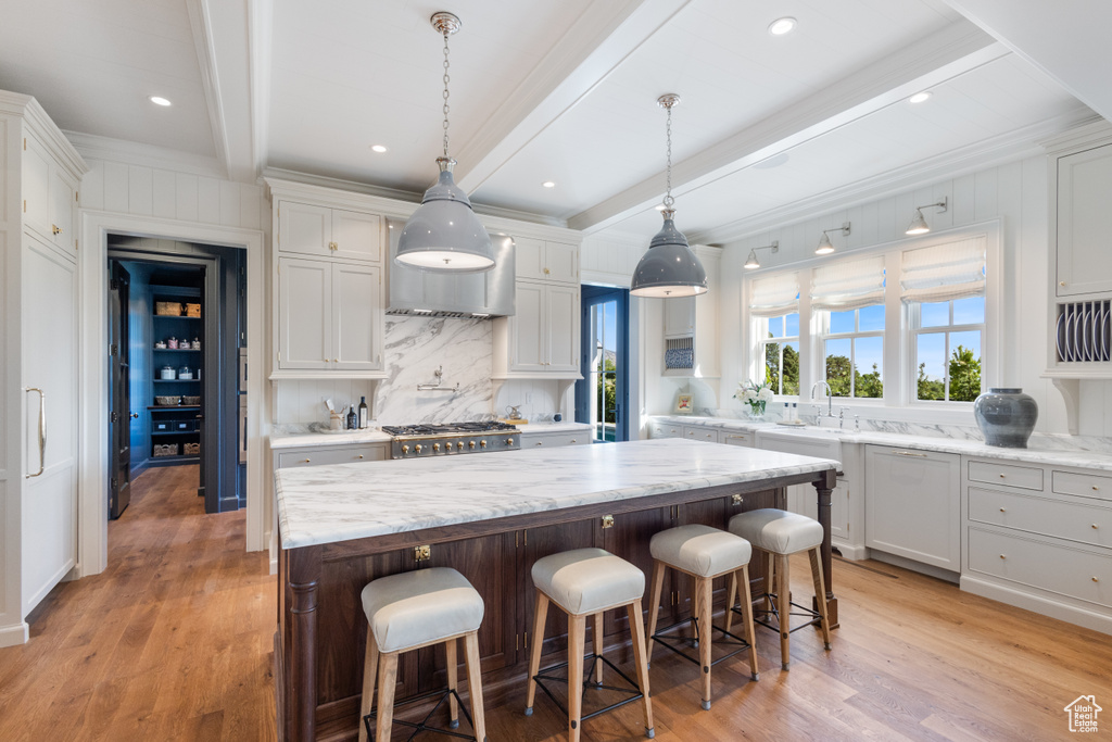 Kitchen with decorative backsplash, beamed ceiling, a center island, light wood-style floors, and white cabinets