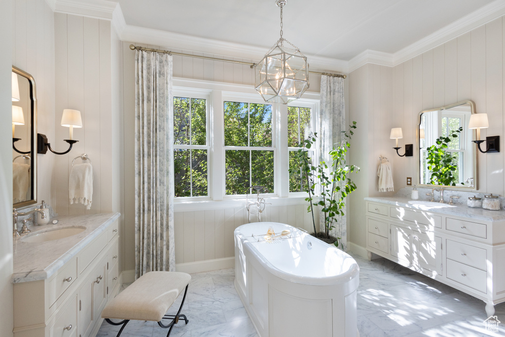 Full bath with marble finish flooring, crown molding, two vanities, a freestanding bath, and baseboards
