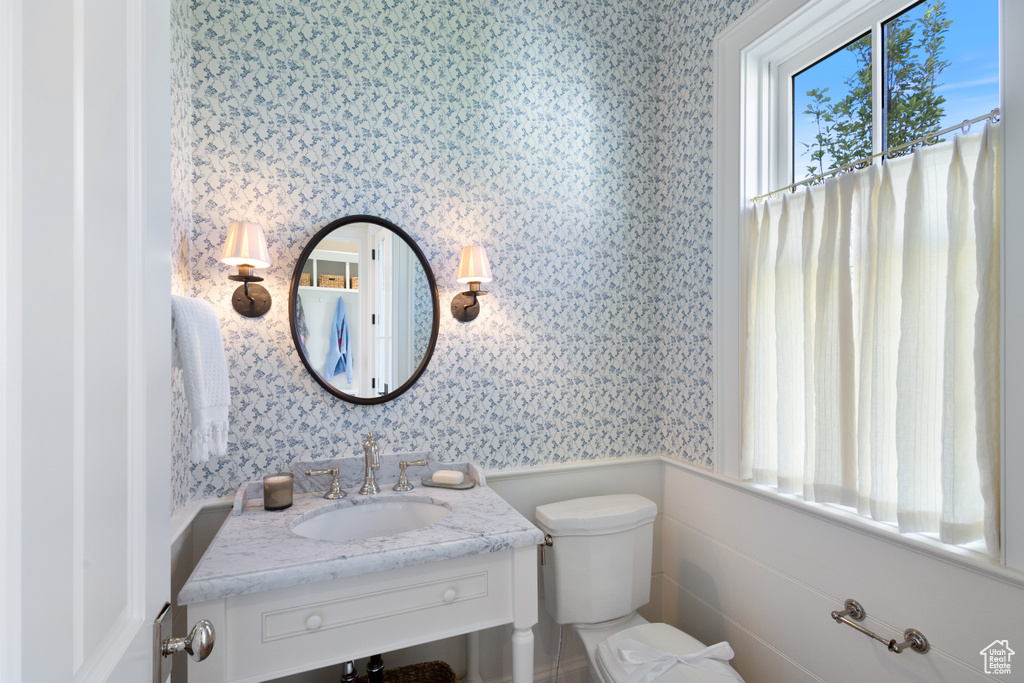 Bathroom featuring wallpapered walls, toilet, vanity, and a wainscoted wall
