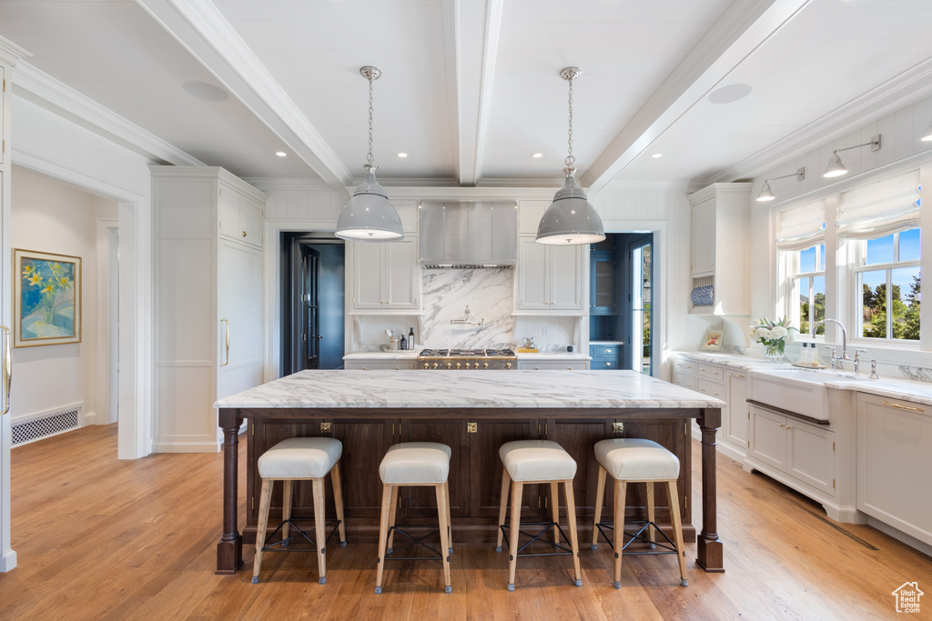 Kitchen featuring a sink, range hood, white cabinetry, beam ceiling, and light wood finished floors