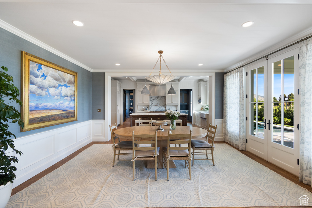 Dining area featuring ornamental molding, light wood-style floors, wainscoting, french doors, and a decorative wall