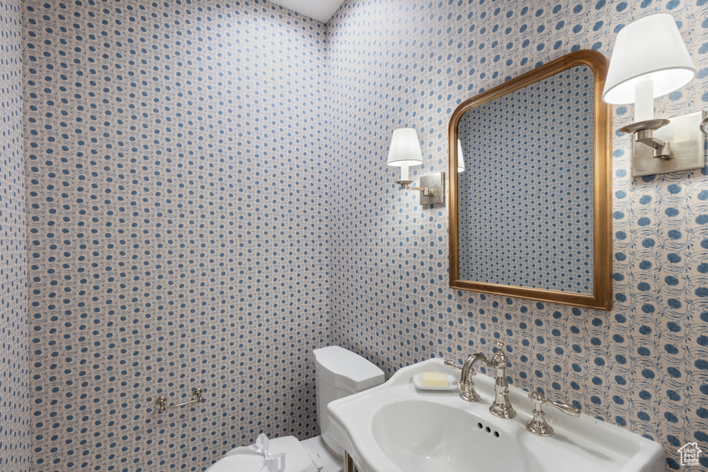 Bathroom featuring toilet, a sink, and wallpapered walls