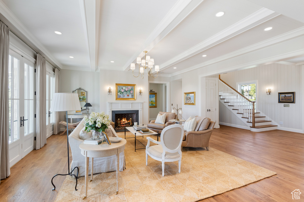 Living room featuring stairs, wood finished floors, a warm lit fireplace, beamed ceiling, and ornamental molding