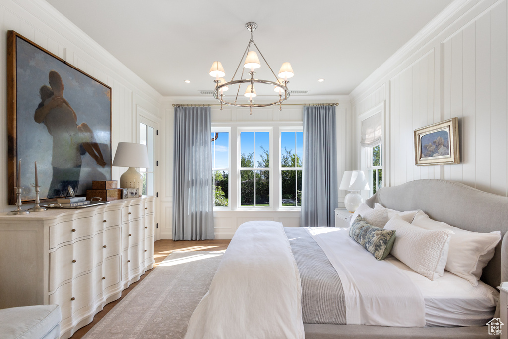 Bedroom featuring a chandelier, ornamental molding, wood finished floors, and a decorative wall