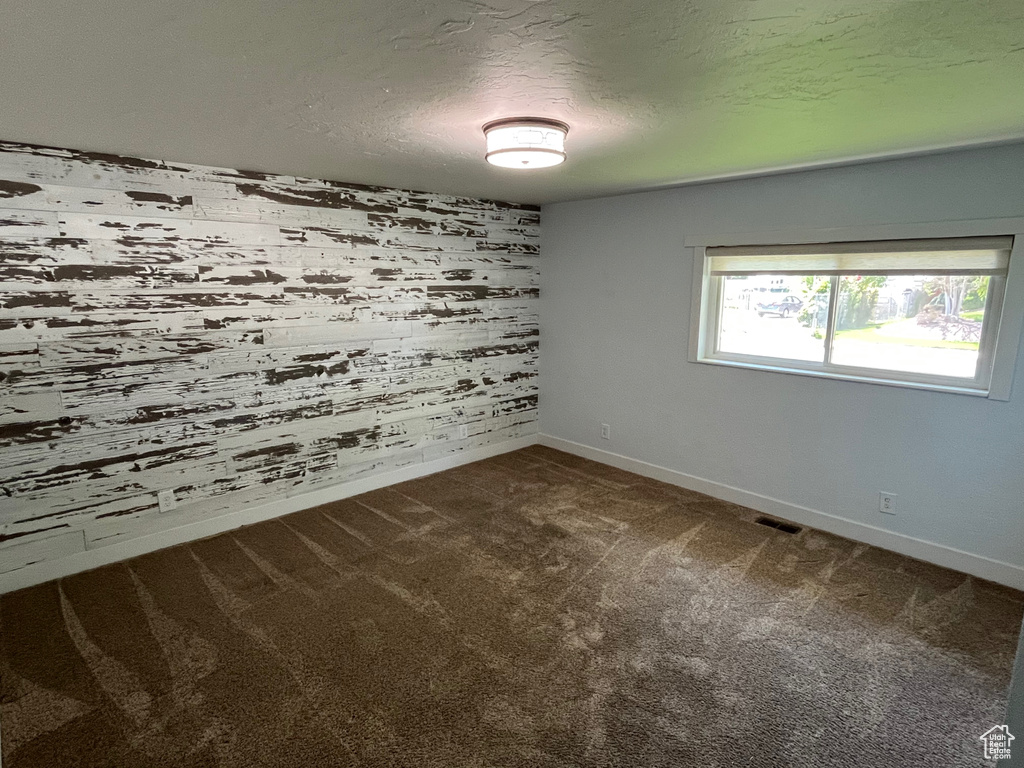 Unfurnished room featuring dark colored carpet, baseboards, wooden walls, and a textured ceiling